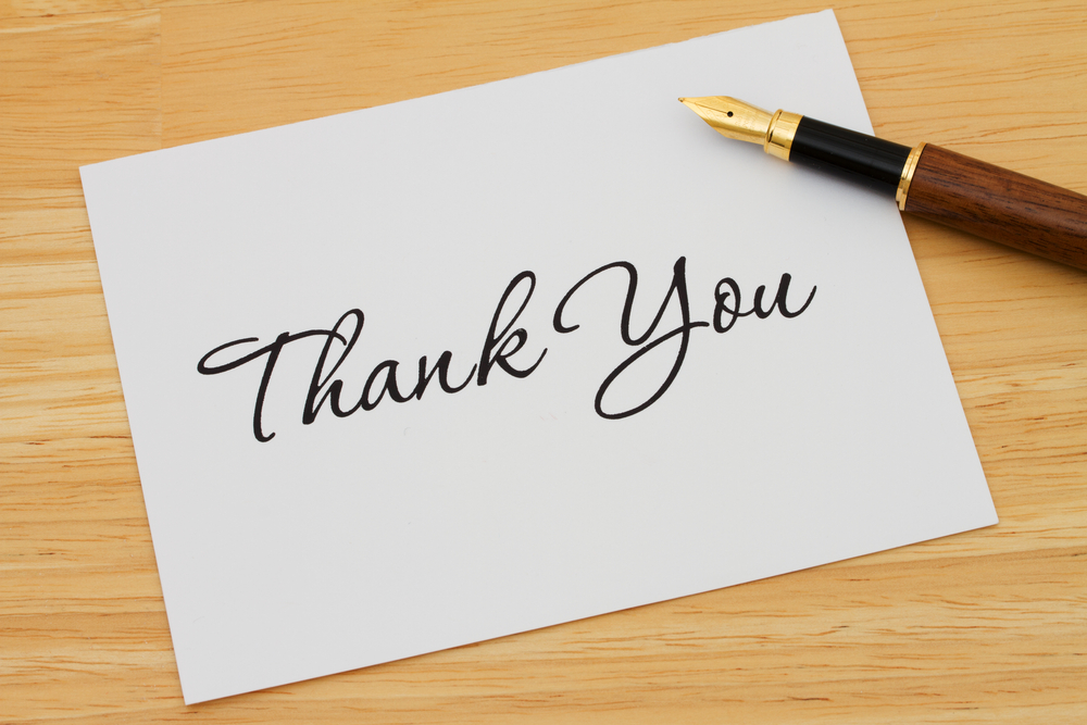 Note card that says thank you with a pen